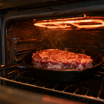 Steak broiling under oven heat with glowing broiler element