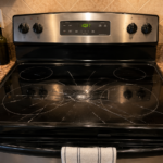 Cracked glass cooktop on kitchen range with fracture spreading across burner zones