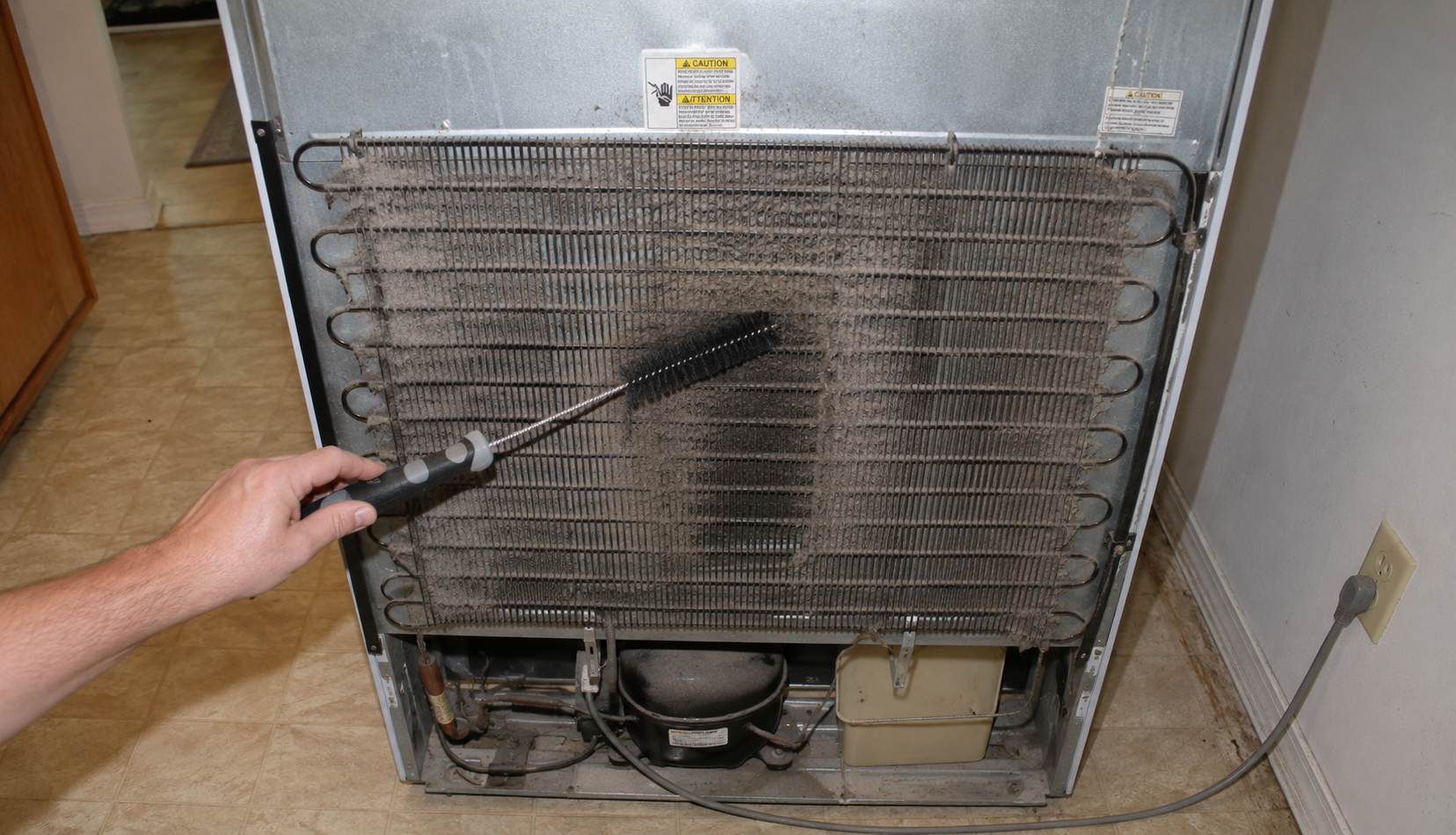 dirty refrigerator condenser coils being cleaned with brush