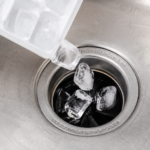 Ice cubes being poured down garbage disposal drain for cleaning