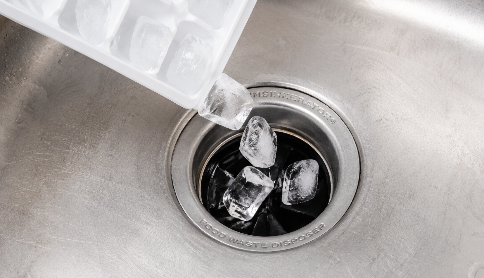 Ice cubes being poured down garbage disposal drain for cleaning