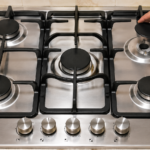 Hand lifting burner cap off gas stove cooktop to begin cleaning process