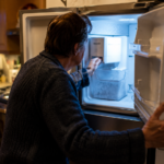 Person checking a broken ice maker inside an open freezer at home