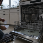 Bosch dishwasher open with standing water in the tub and a person bailing it out