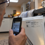 Man photographing the model number label on a Whirlpool dishwasher door edge