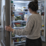Woman checking a milk carton inside an open refrigerator that may not be cooling